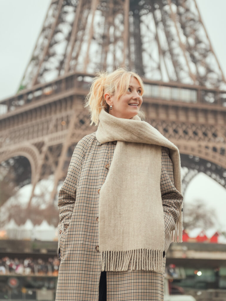 Woman in a checked coat and cream scarf near the Eiffel Tower