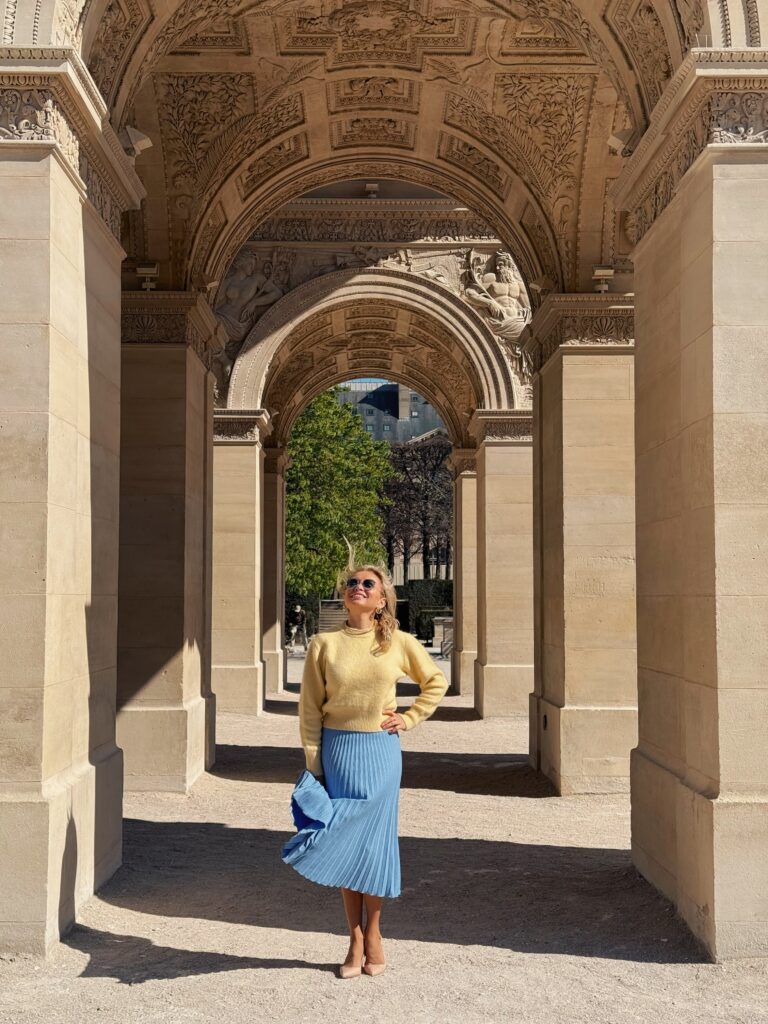 Solo portrait in a yellow top and blue skirt beneath a stone arch in Paris