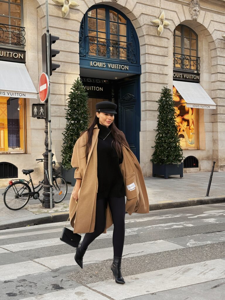 Woman walking across a Paris street in a camel coat and black trousers
